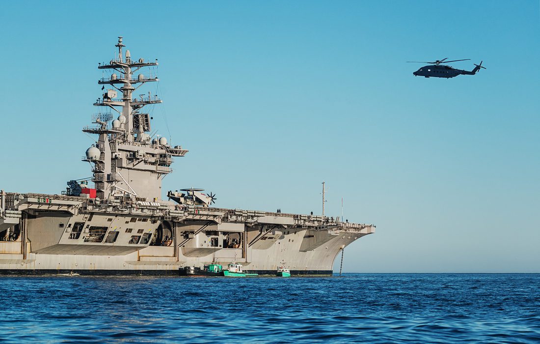 Aircraft carrier with helicopter flying nearby.
