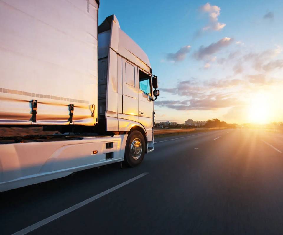 Truck driving on highway at sunset.